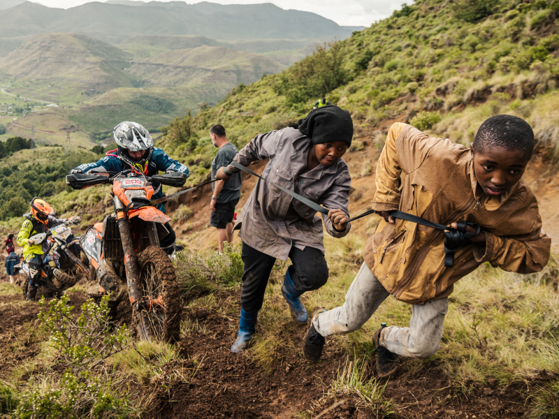 Pilotos recebem ajuda dos locais para subir uma secção íngreme das montanhas do Lesoto durante o enduro Roof of Africa.